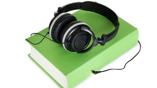 Black headphones sitting on top of green book, seemingly plugged into book