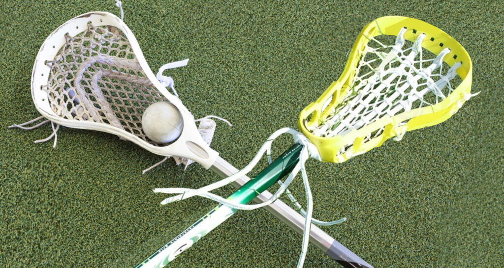 Two lacrosse sticks on the ground, one holding a ball