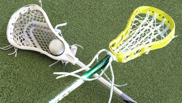 Two lacrosse sticks on the ground, one holding a ball