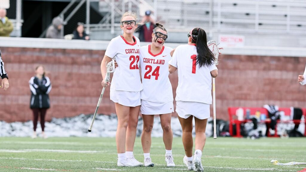 Three members of the Women's Lacrosse Team gather on the field smiling