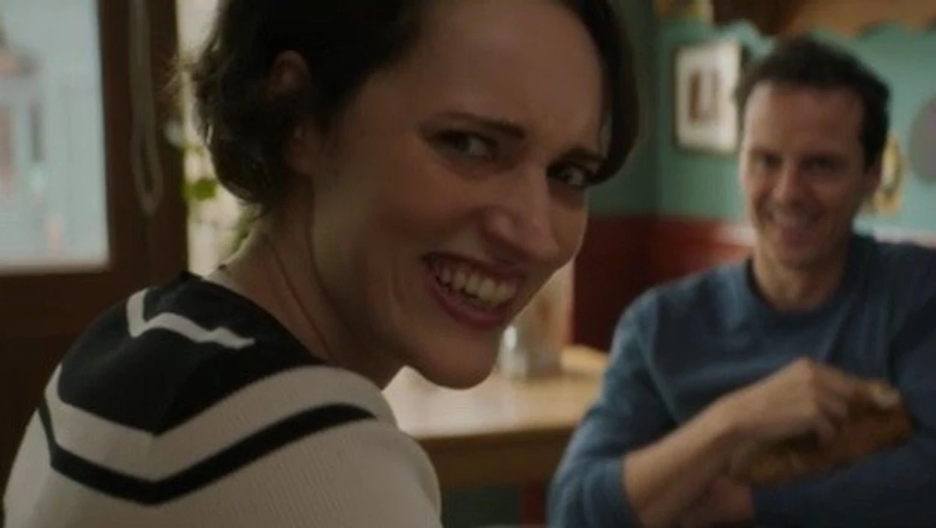Fleabag and The Priest sitting in her cafe. Fleabag is in the camera’s focus and the Priest is not. They both are smiling but Fleabag’s smile has a worried and confused subtext.