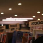 Photo of a bookstore interior with focus on a 'Psychology' section sign. Other category signs are visible but blurred in the background.