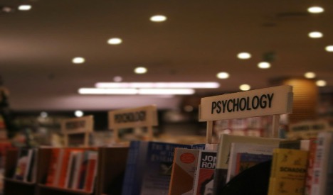 Photo of a bookstore interior with focus on a 'Psychology' section sign. Other category signs are visible but blurred in the background.