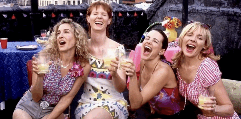 Four women seated laughing holding drinks.
