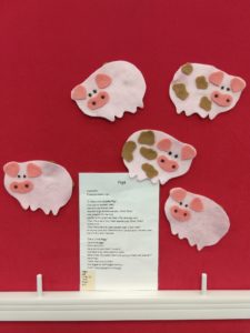 A red flannel board with a TMC flannel kit containing three clean, pink felt pigs and two dirty, pink felt pigs.