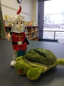 A puppet knight in red armor and a sword standing over a green puppet turtle--two puppets from TMC’s puppet collection