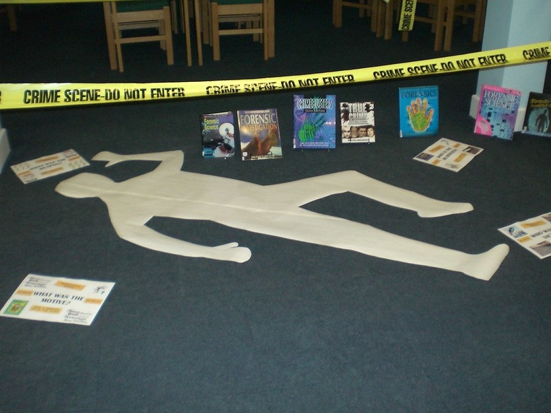 :  Image by bl_library from Flickr.  Image of the outline of a body on the floor, surrounded by crime scene caution tape and library books